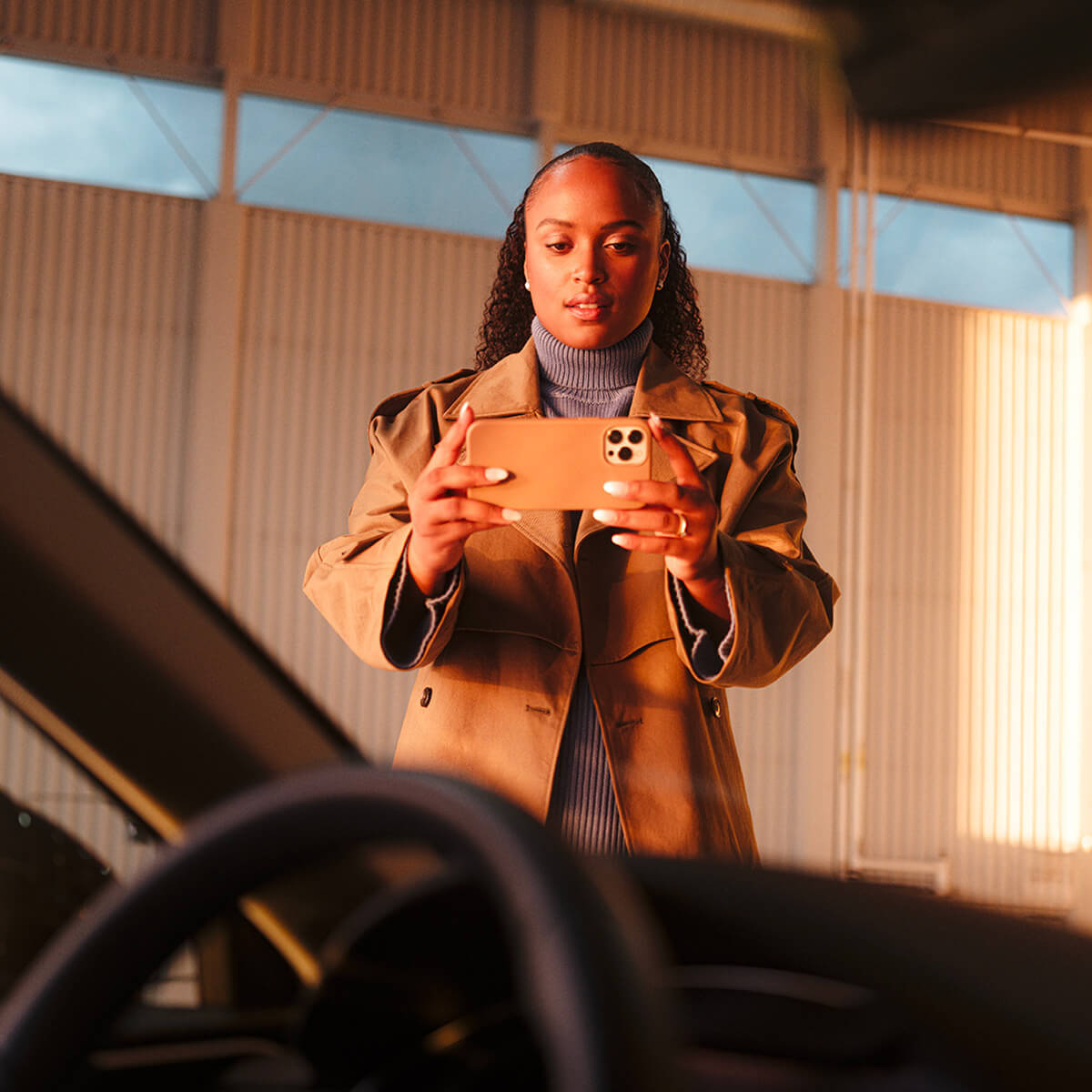 Looking out the car windshiled from the passenger's seat, a woman is using PAVE on their phone to inspect the car